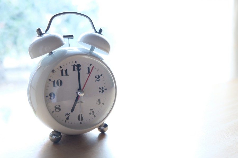 明るい窓辺に置かれた、7時を指すアナログ目覚まし時計。