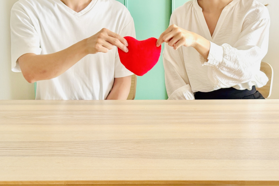 テーブルに座り、二人でハートの形を持つ男女の手元