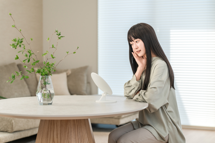 部屋で鏡を見ながら肌の調子を確かめる女性