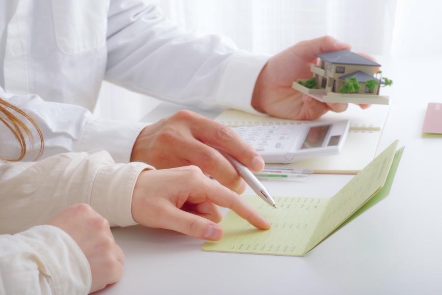 家にミニチュア模型を手に通帳を見ながら電卓を弾く夫婦の手元