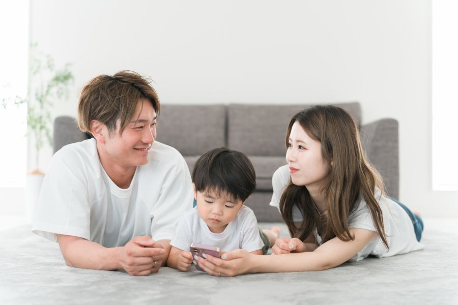 床に寝そべって話をする若い夫婦と子ども