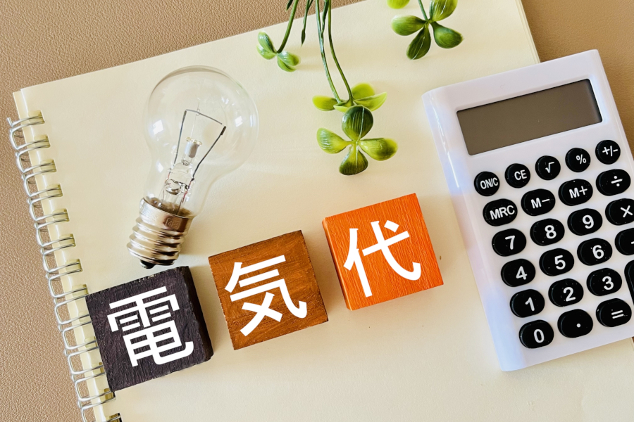ルーズリーフの上に置かれた電卓と電球、電気代の文字